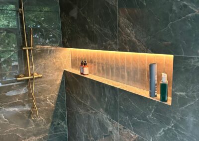 Luxe inloopdouche met groene marmeren wanden, een geïntegreerd schap in de wand en sfeervol LED-licht, vakkundig geïnstalleerd door Nervabouw en Kozijnen voor een elegante en functionele badkamer.